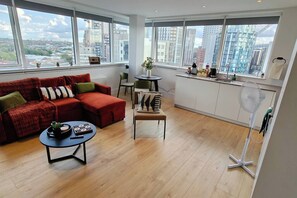 Un soggiorno moderno con un divano rosso, un tavolino da caffè e vista sulla città tramite ampie finestre.