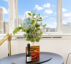 Un tavolo con una bottiglia di vino, una scatola di bicchieri da vino, una pianta in vaso e una finestra con vista sulla città e su un ponte.