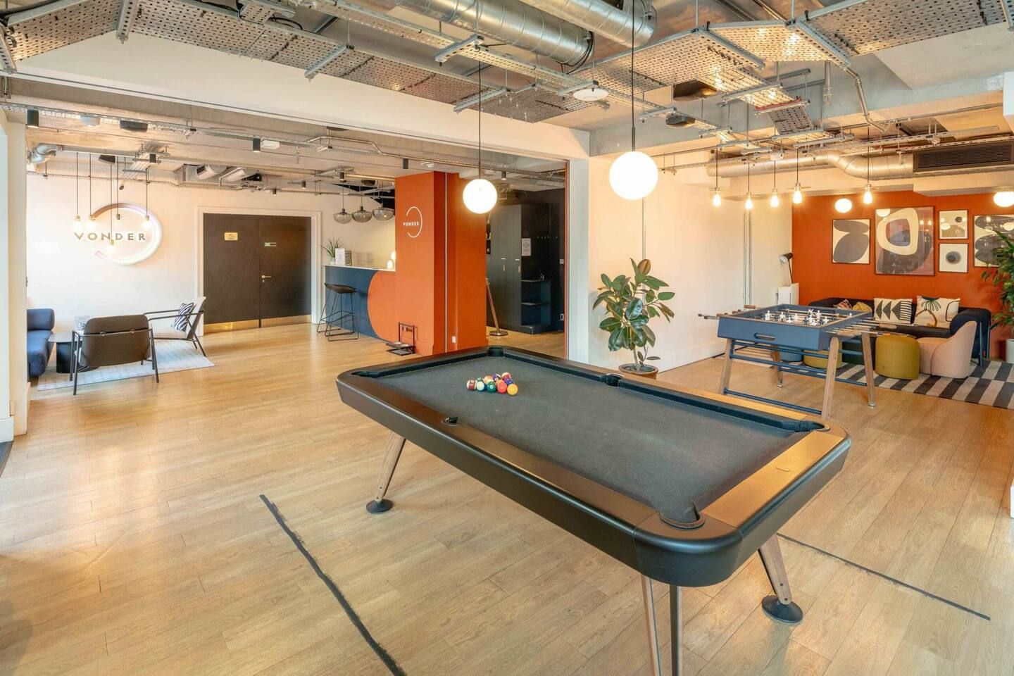 Ein Billardtisch in einem modernen Innenraum mit Holzboden, einer Couch und einem Kicker.