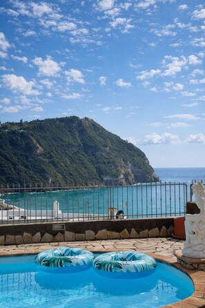 A swimming pool with inflatable rings, a statue, and a view of a coastal landscape with a mountain. - Alvillino, Ischia - Sea View Villa with Private Pool (Forio)