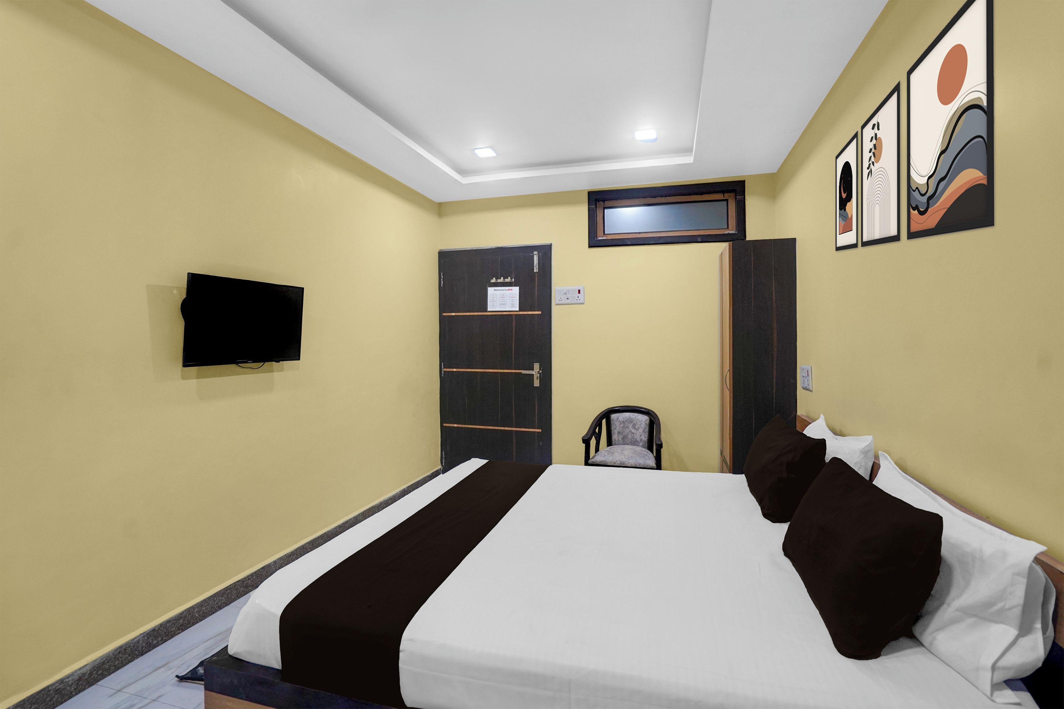 A hotel room with a bed, a television mounted on the wall, a door, and a window.