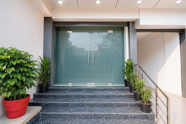 Entrada de um edifício moderno com porta de vidro, degraus de mármore e plantas em vasos.