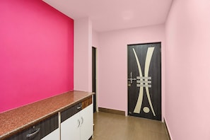 A hallway with a pink wall, a wooden door with a unique design, and a counter with drawers. - Hotel Rudransh Residency (Adityapur)