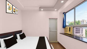 A hotel room with a bed, a window with a view, a door, and framed artwork on the wall.