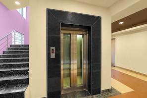 An elevator in a building with a marble floor and a staircase with metal railings. - Hotel Rudransh Residency (Adityapur)