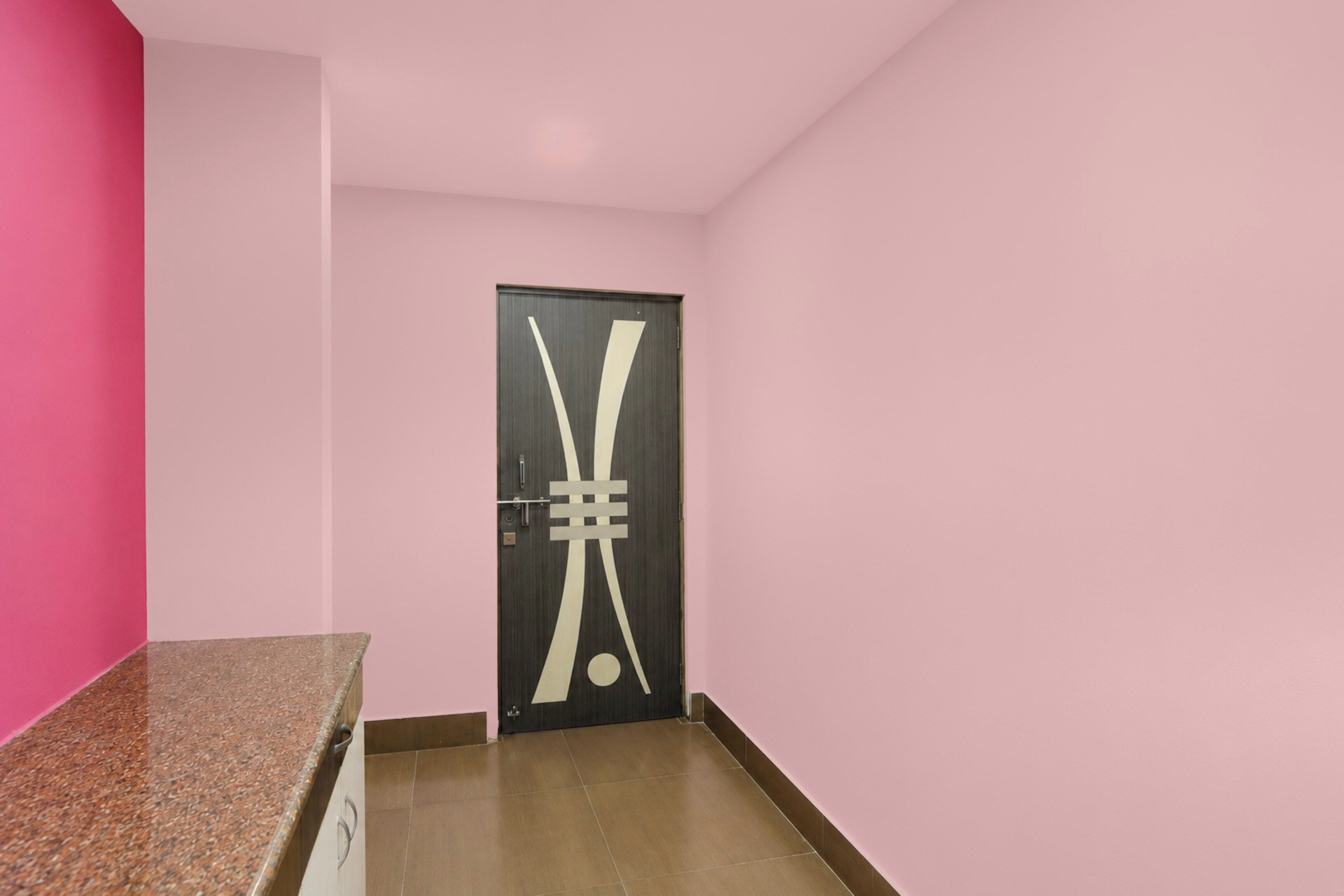 Een gang met een roze muur, een deur met een geometrisch ontwerp, en een bruine vloer.