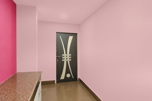 A hallway with a pink wall, a door with a geometric design, and a brown floor.