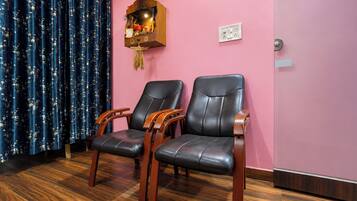 A room with two leather chairs, a wooden shelf with decorative items, a clock on the wall, and a power outlet.