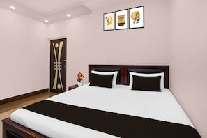 A hotel room with a large bed, a nightstand, a vase with flowers, and three framed artworks on the wall.