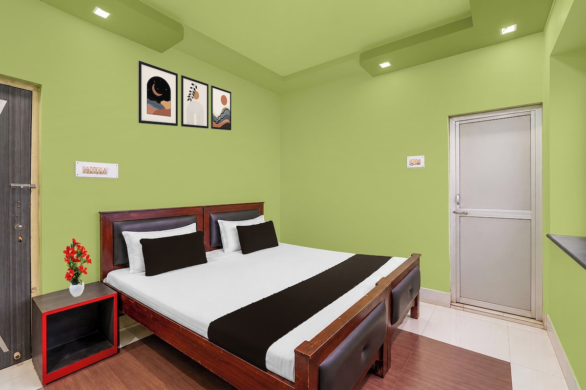 A hotel room with a bed, a bedside table with a vase of flowers, and a door.