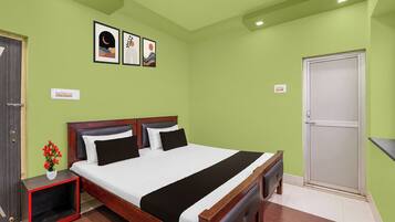 Una habitación de hotel con una cama, una mesita de noche con un florero y una puerta.