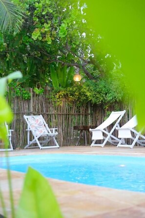 A swimming pool with lounge chairs and a bamboo fence.