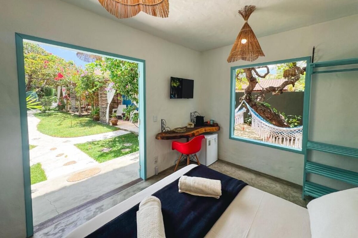 A bedroom with a bed, a desk, and a chair, a TV, and a view of a garden.