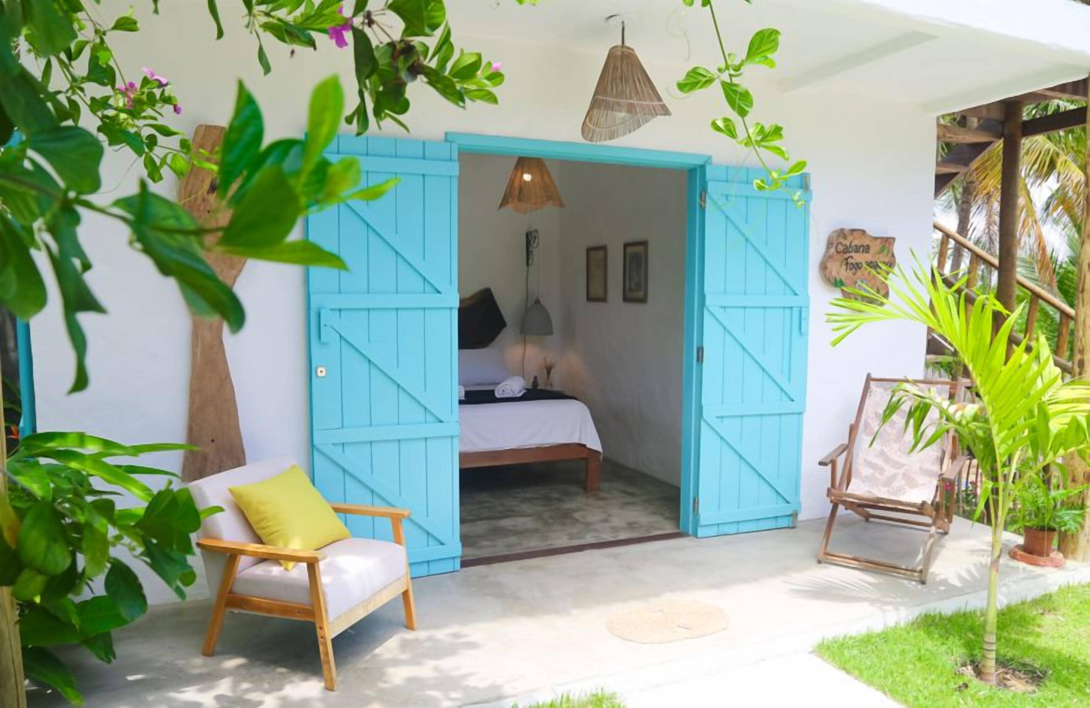 Quarto com uma cama, uma cadeira e uma porta azul que dá para outro quarto.