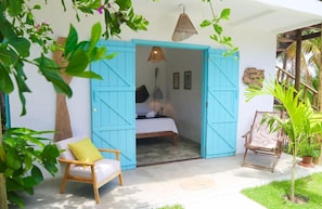 A room with a bed, a chair, and a blue door leading to another room. - Casa Peroá Pousada (Amontada)
