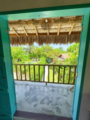 An open doorway leading to a balcony with a thatched roof and a view of a lush garden.