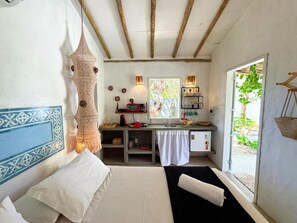 A bedroom with a bed, a desk, a hanging lamp, and a window with a view of greenery. - Casa Peroá Pousada (Amontada)