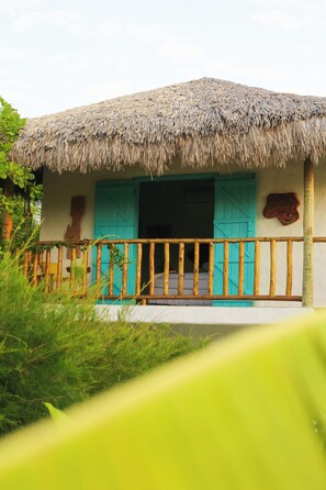 A thatched-roof structure with a wooden balcony and turquoise shutters.