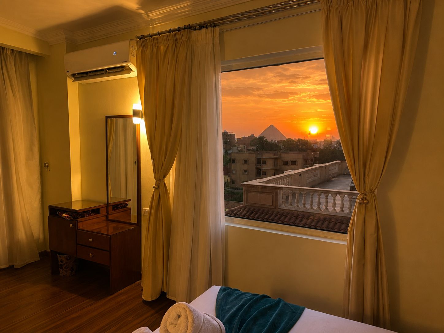 A hotel room with a bed, a wooden dresser, a mirror, and a window with curtains.