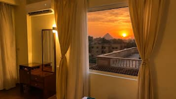 A hotel room with a bed, a wooden dresser, a mirror, and a window with curtains.