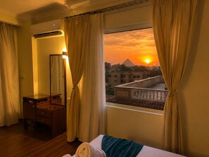 Una habitación de hotel con una cama, un aparador de madera, un espejo y una ventana con cortinas.
