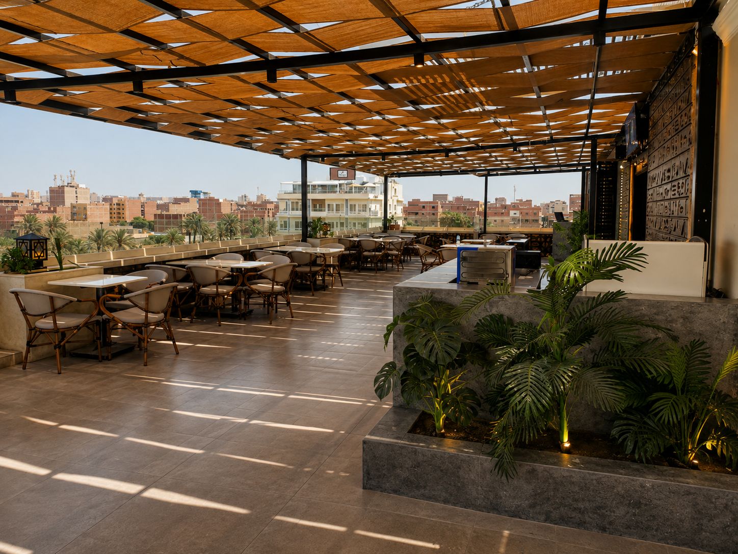Un área de estar al aire libre con mesas y sillas, una pérgola en lo alto y una vista panorámica de la ciudad de fondo.