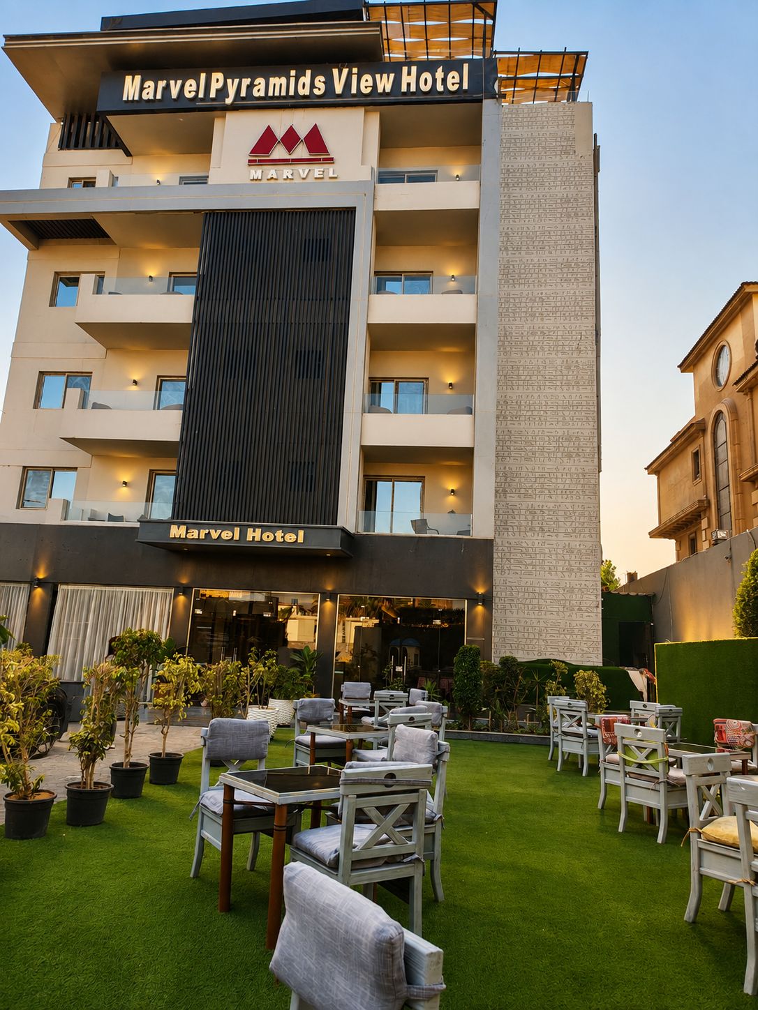 Un hotel con fachada moderna, zona de estar al aire libre y un letrero que dice 'MarvelPyramids View Hotel'.