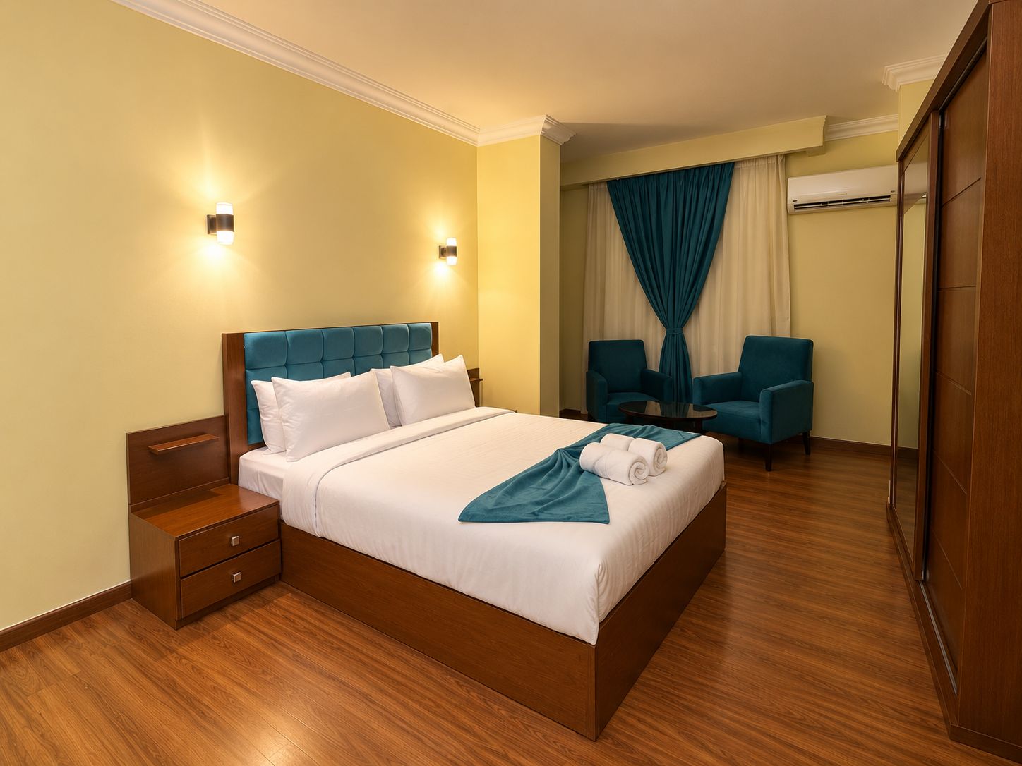 Una habitación de hotel con una cama grande, dos mesitas de noche, un escritorio, dos sillas y un armario.