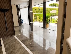Un vestíbulo moderno con una puerta de cristal que da a un área exterior, una silla azul y una planta en maceta.