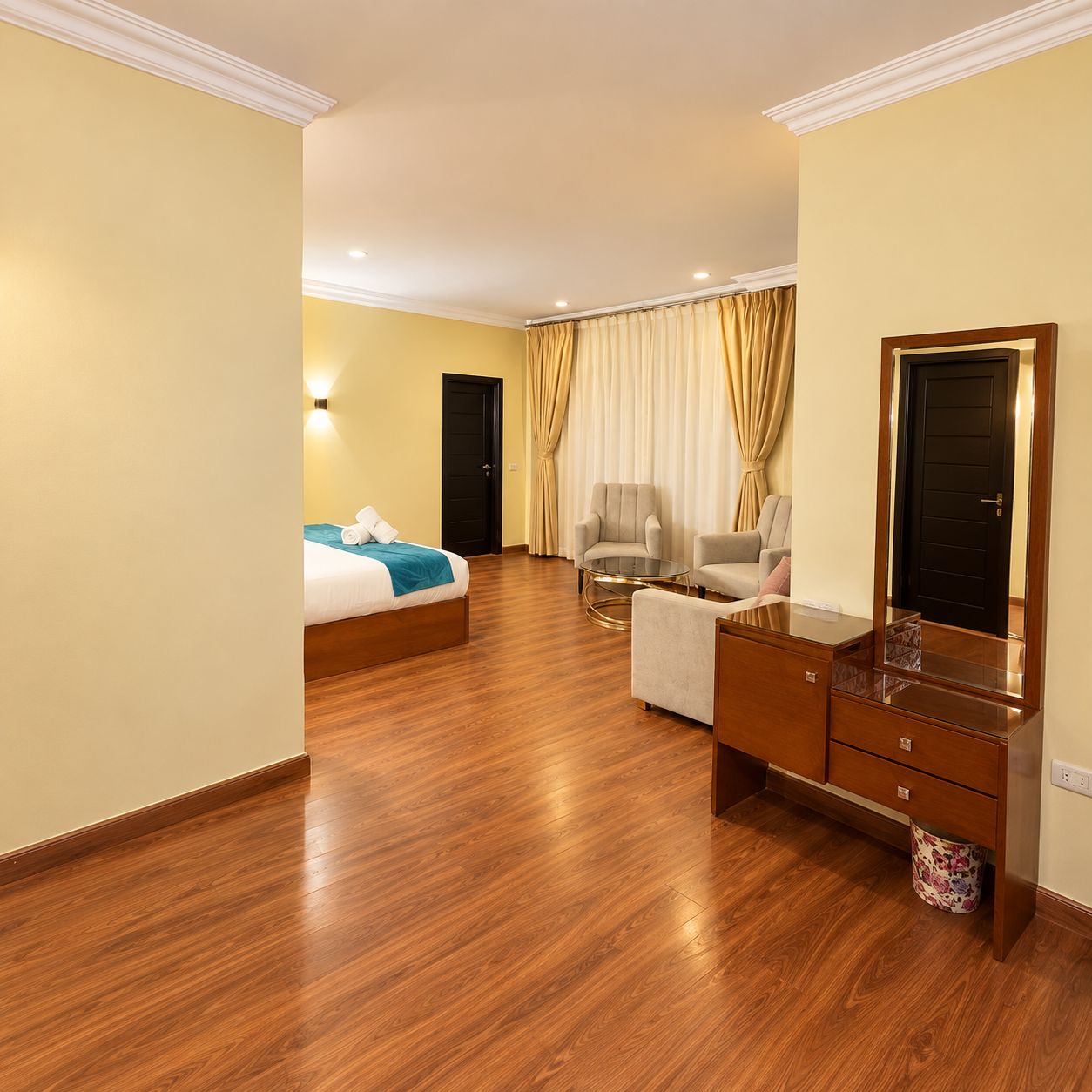 A hotel room with a bed, two armchairs, a small table, a mirror, and a wardrobe.