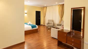 A hotel room with a bed, two armchairs, a small table, a mirror, and a wardrobe.