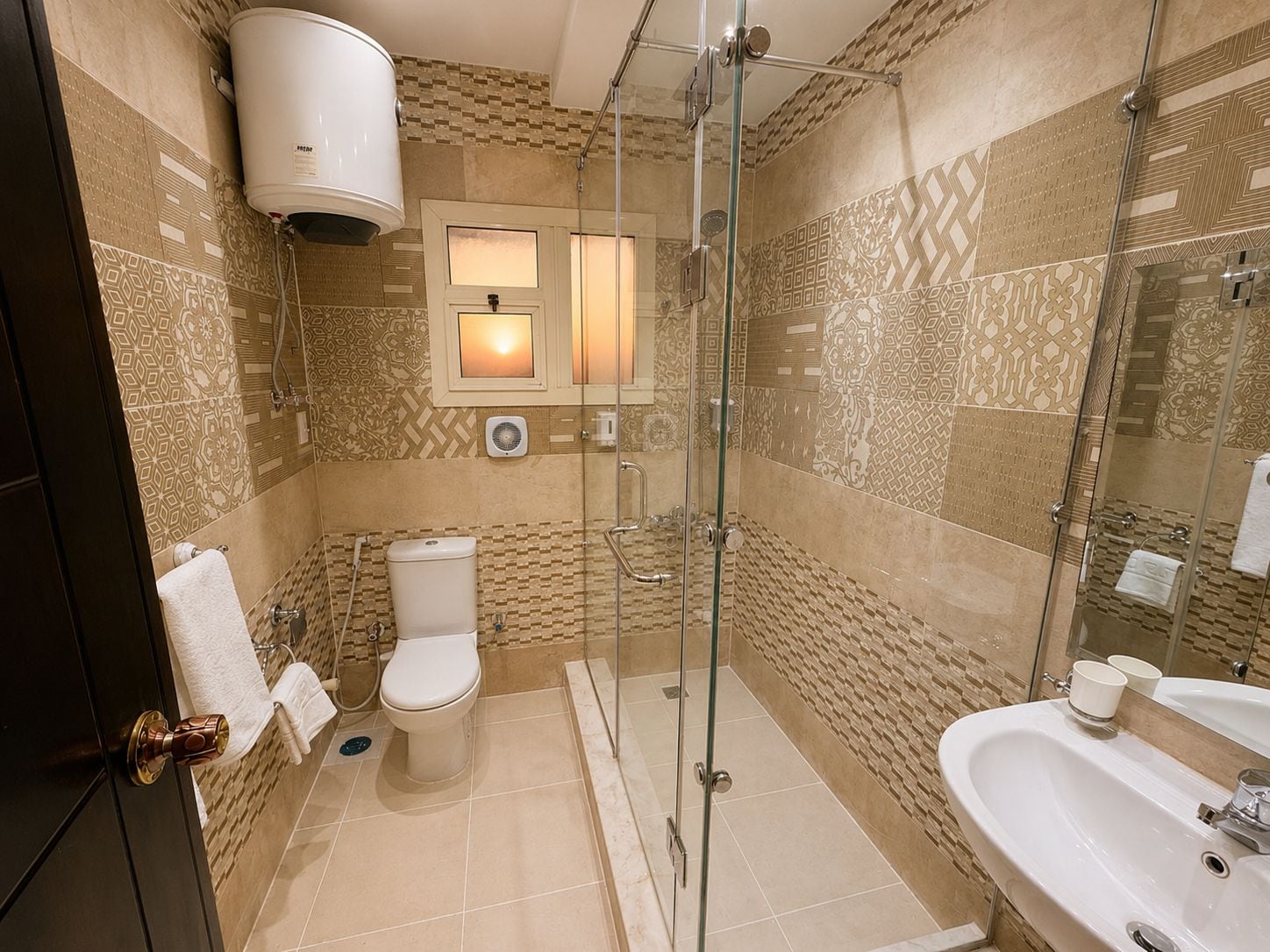 Un baño con ducha de vidrio, inodoro, lavamanos y perchero para toallas.