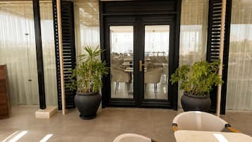 Ein modernes Interieur mit einer Tür mit schwarzem Rahmen, zwei Zimmerpflanzen und einer Sitzecke inklusive Tisch und Stühlen.