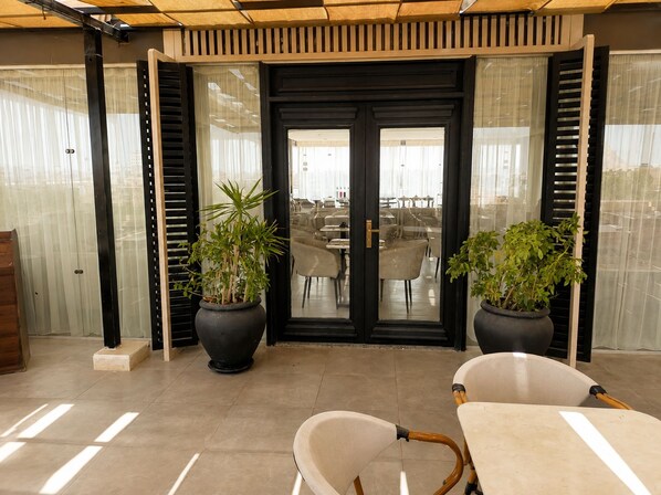 Un interior moderno con una puerta de marco negro, dos plantas en macetas y una zona de estar con mesa y sillas.