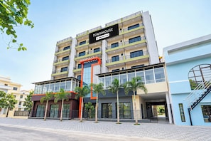 A multi-story building with balconies, a prominent entrance, and a sign indicating it is serviced by OYO.