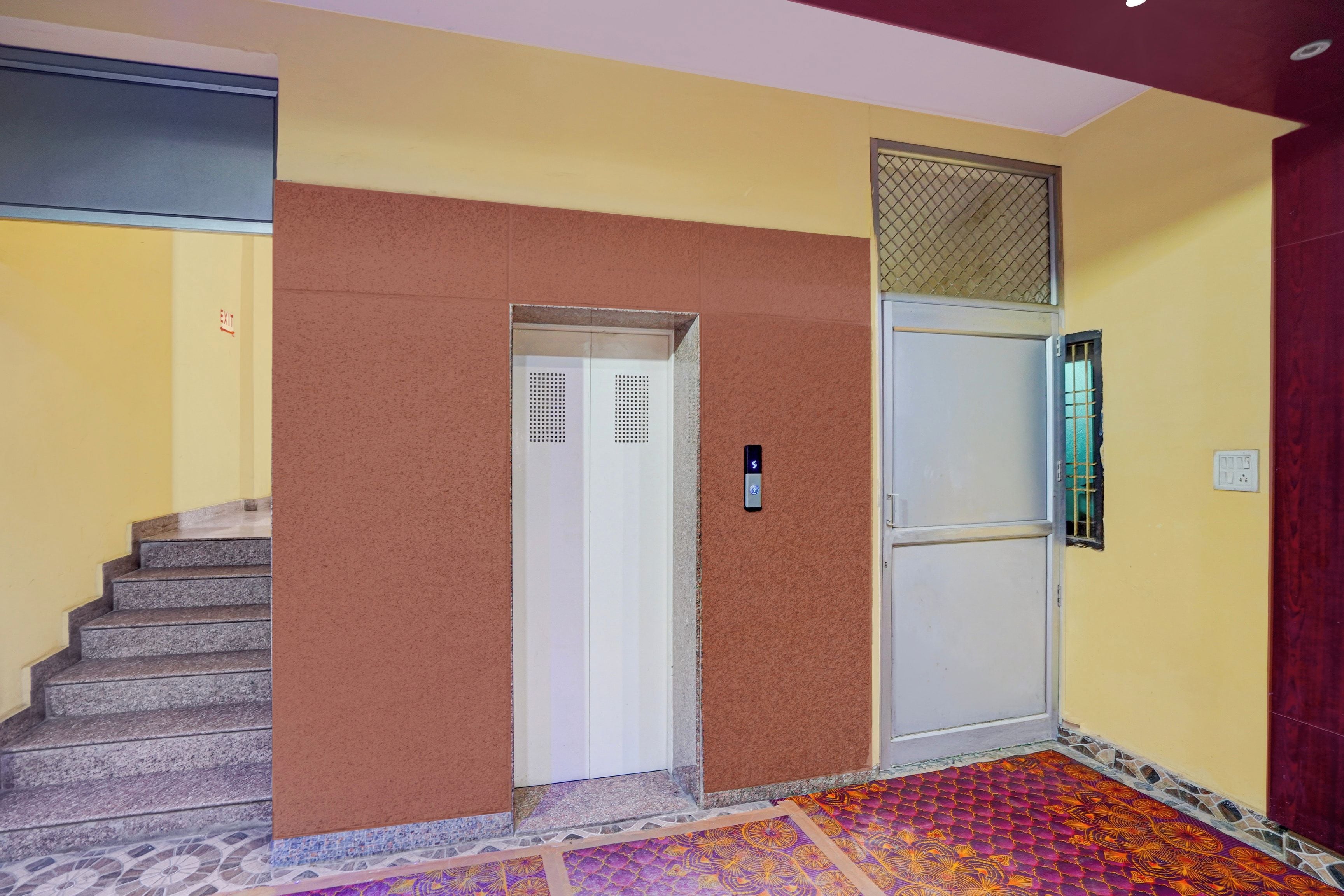 Escada que dá acesso a um elevador, porta com teclado numérico e carpete estampado.