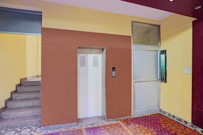 Una escalera que sube a un ascensor, una puerta con teclado numérico y una alfombra estampada.