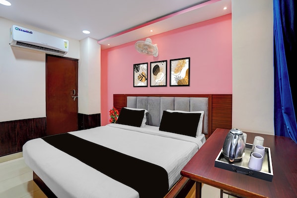 Habitació d'hotel amb un llit, una taula de nit amb una paperera i tasses, aire condicionat fixat a la paret i una porta.