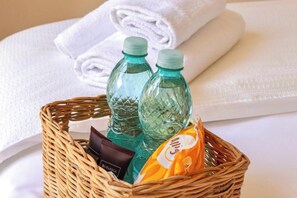 A wicker basket containing two clear plastic water bottles, a brown toiletry bag, and a yellow snack packet. - Alba Guest House (Cagliari)