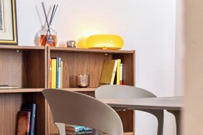 A room with a wooden bookshelf, a white chair, and a table. - Alba Guest House (Cagliari)