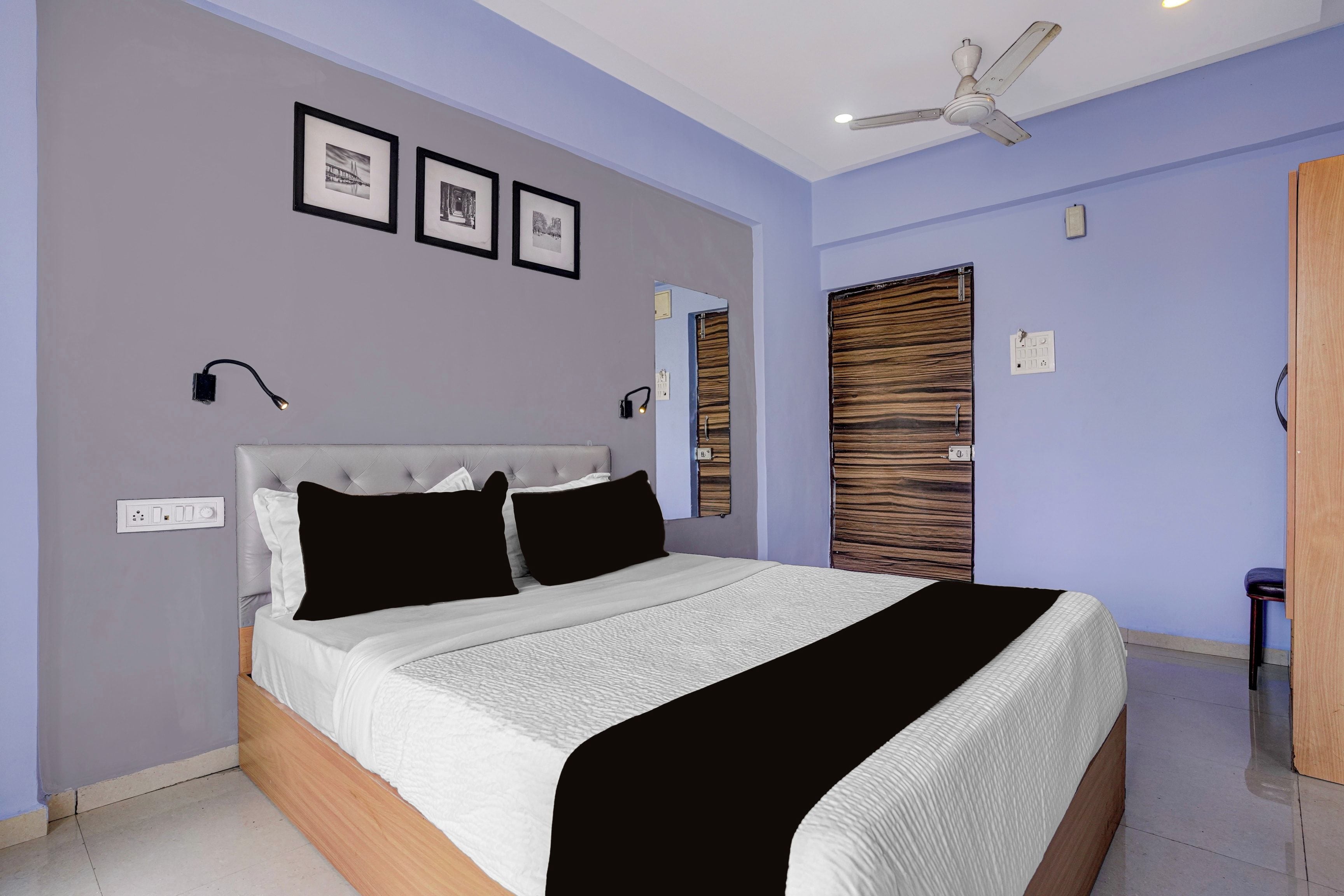 A bedroom with a bed, ceiling fan, wall-mounted light, and framed pictures.