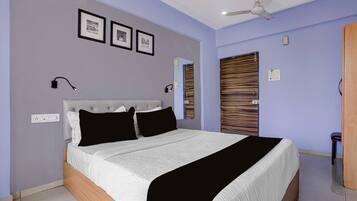 A bedroom with a bed, ceiling fan, wall-mounted light, and framed pictures.