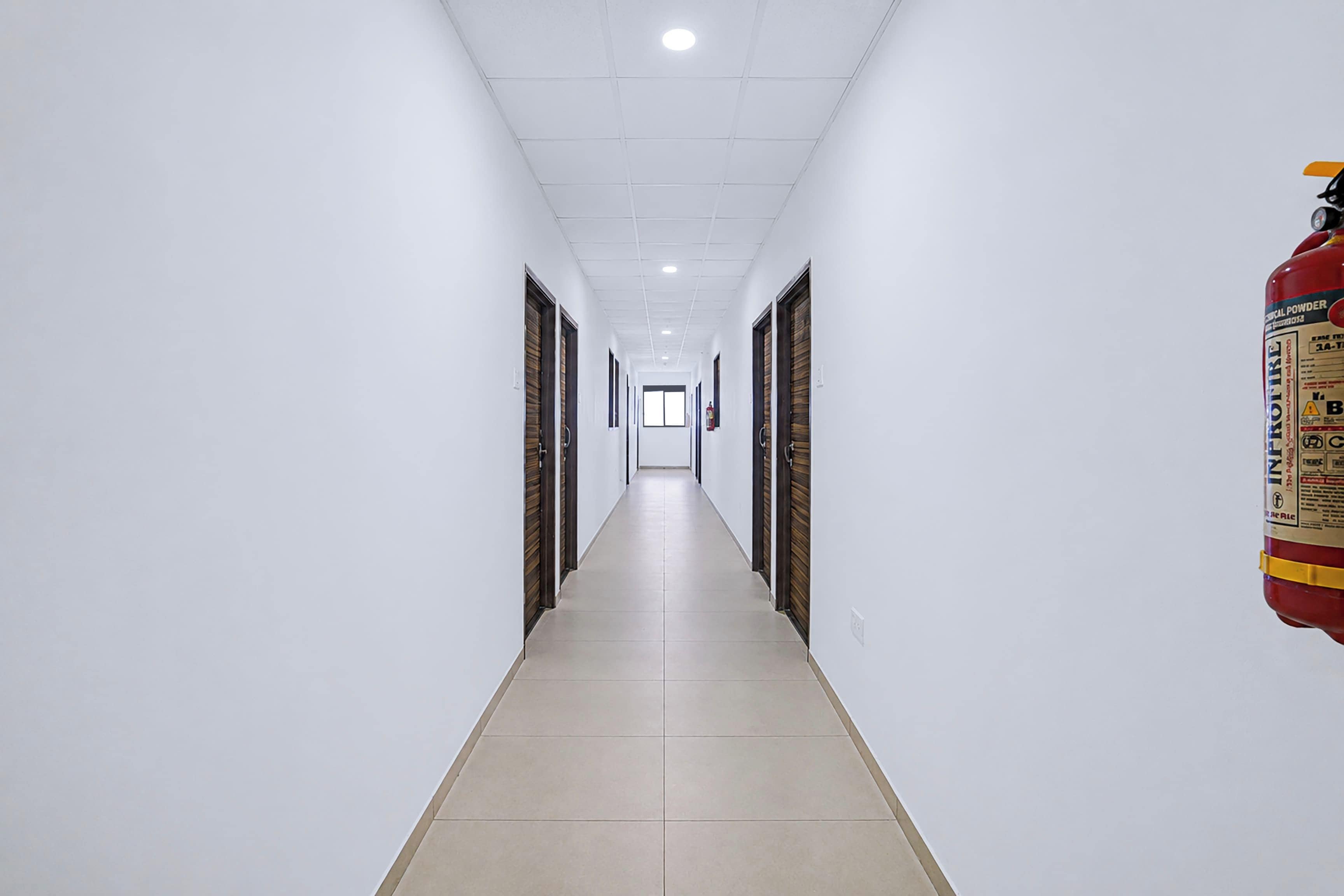 Un pasillo largo y estrecho con paredes blancas y piso de baldosas, que conduce a una puerta al final.