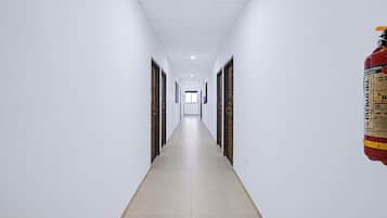 Un pasillo largo y estrecho con paredes blancas y piso de baldosas, que conduce a una puerta al final.