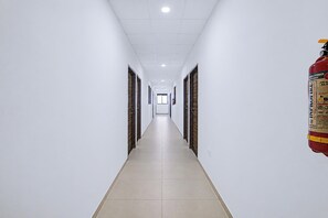 A long, narrow hallway with white walls and a tiled floor, leading to a door at the end.