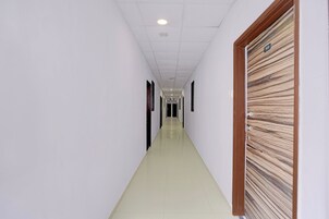 A corridor with white walls, a tiled floor, and a door with a wood-like panel design.