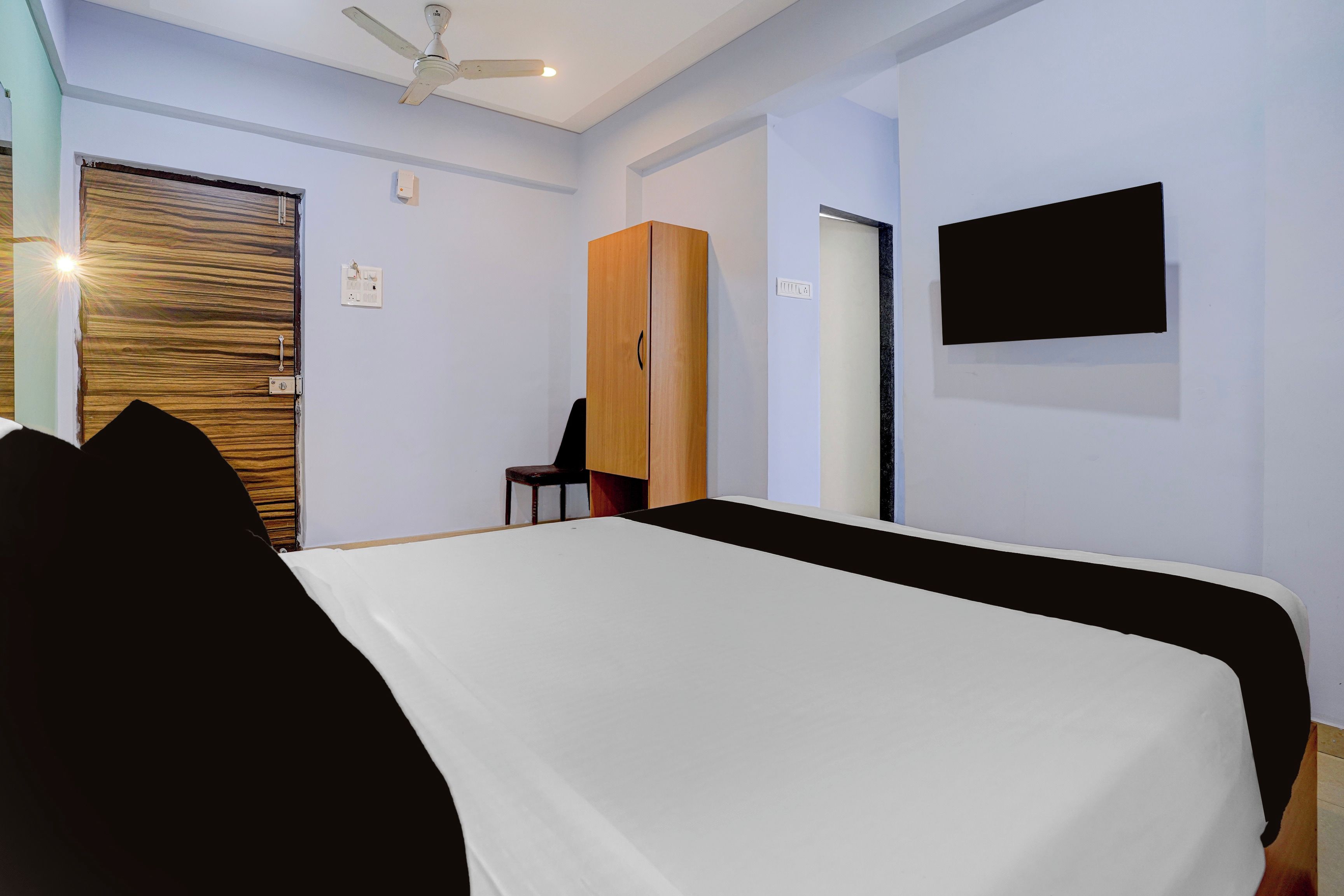 A hotel room with a bed, a wardrobe, a chair, a television, and a ceiling fan.