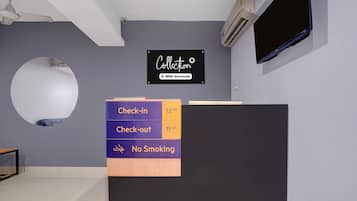 A reception desk with a sign indicating check-in at 12 pm and check-out at 11 am, and a no-smoking policy.