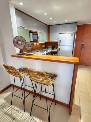 A compact kitchen with a central island, two bar stools, a microwave, a toaster, and a refrigerator. - Spacious 2-Bedroom Apartment | Tressesenta Tower | Punta del Este (Punta del Este)