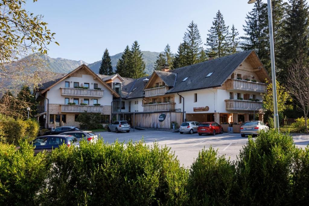 Un hotel con varios balcones, aparcamiento y montañas al fondo.